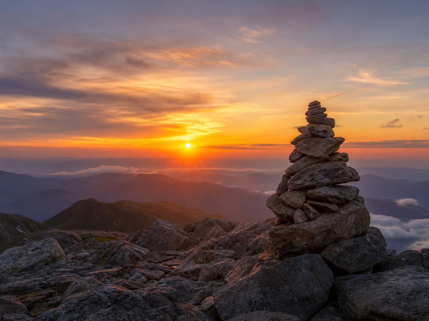 夕焼けの山頂に立つケルン - Summit cairn against an orange sunset sky