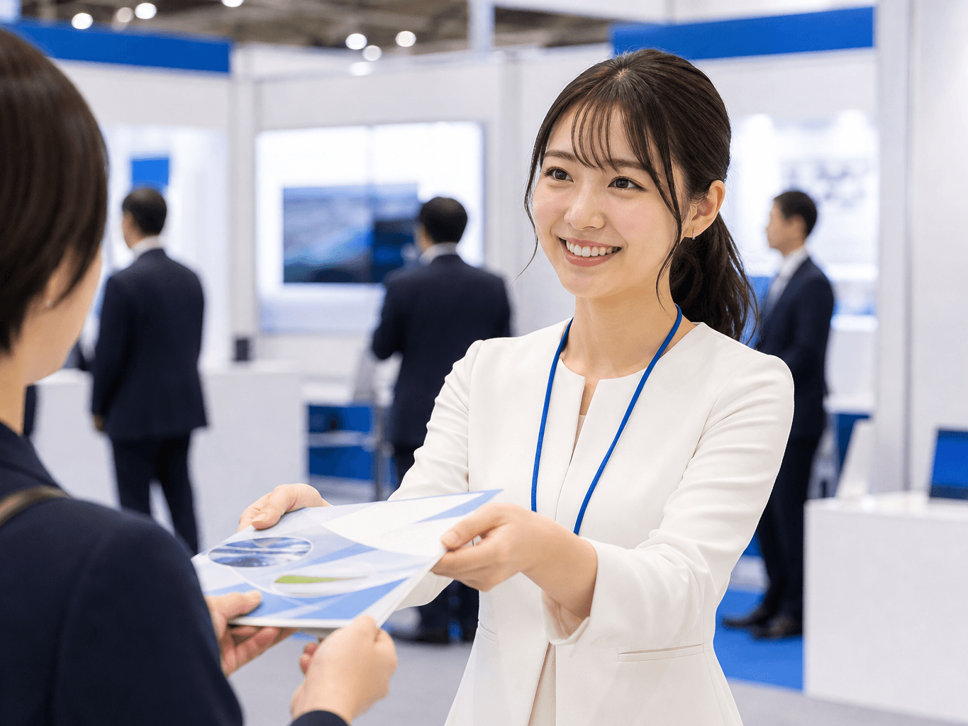 展示会ブースで来場者に製品パンフレットを笑顔で手渡す様子 - Handing Out a Product Brochure at an Exhibition Booth