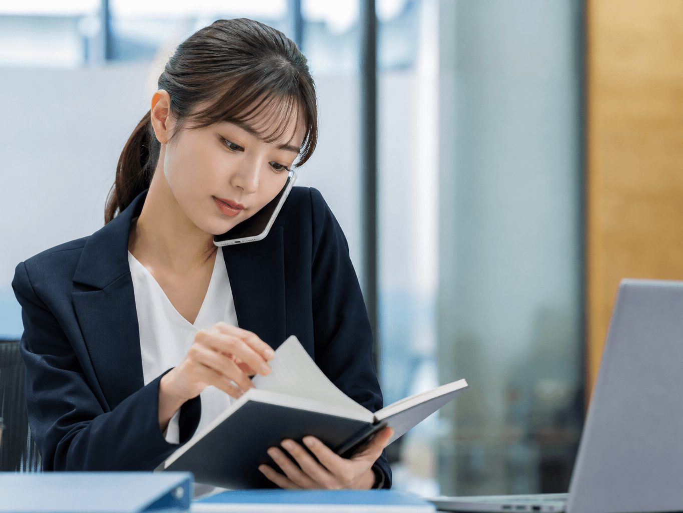 電話対応中にメモ帳をめくる秘書 - Secretary Flipping Through Notepad While on Phone