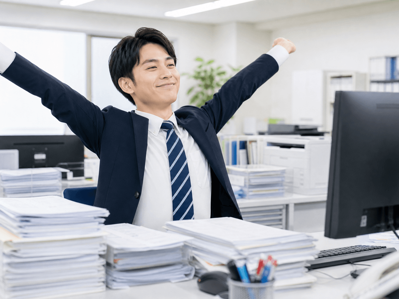 大量の伝票処理を終えてデスクで満足そうに両手を伸ばし伸びをする若手男性社員の様子