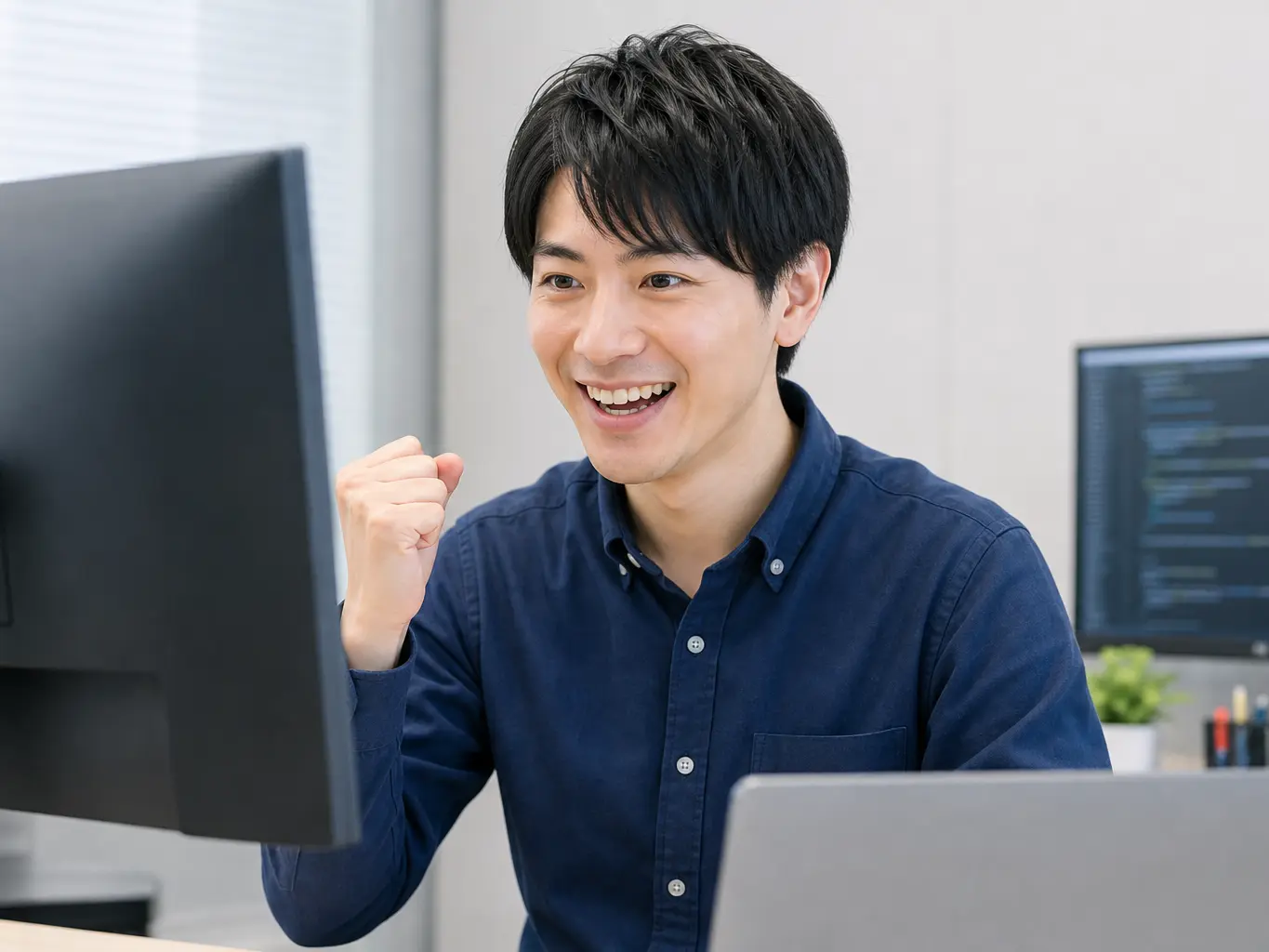 パソコン画面を見て問題解決に歓喜し小さくガッツポーズをする男性エンジニア